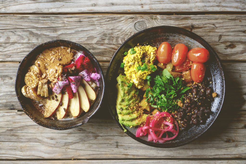 Dos cuencos con fruta, legumbres, quinoa, aguacate y tomates cherry sobre una mesa de madera