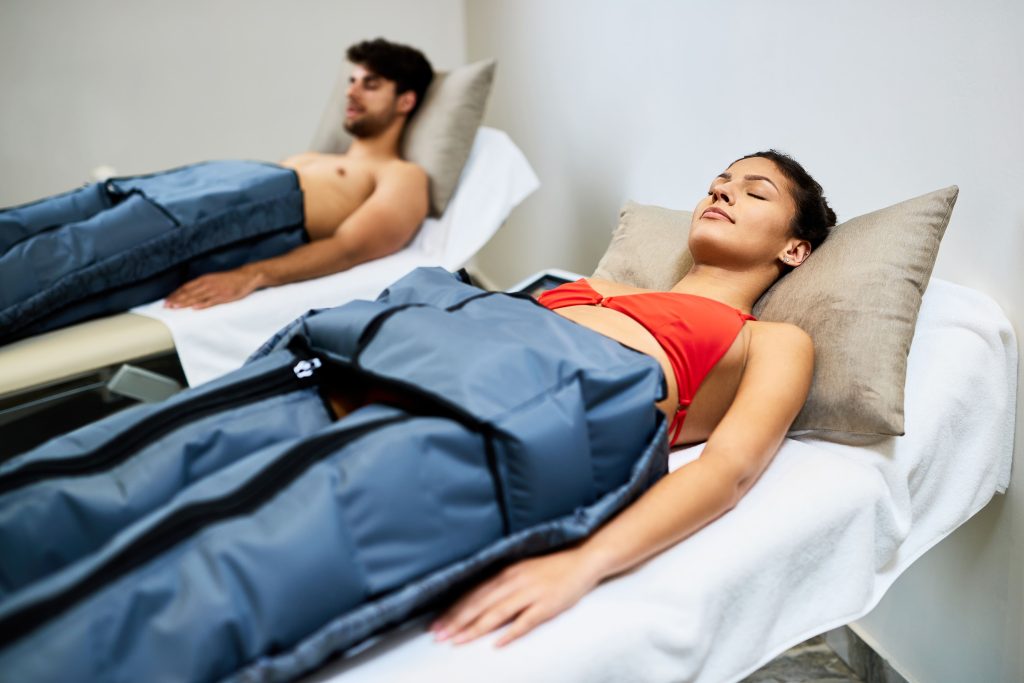 Dos personas relajadas en camillas durante una sesión de presoterapia con botas de compresión